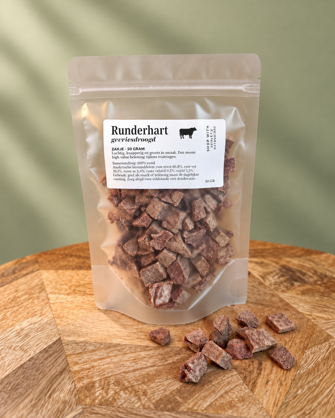 Marley’s gevriesdroogd runderhart 50 gram in een hersluitbaar zakje met losse rundersnacks op houten plateau voor een zachtgroene achtergrond