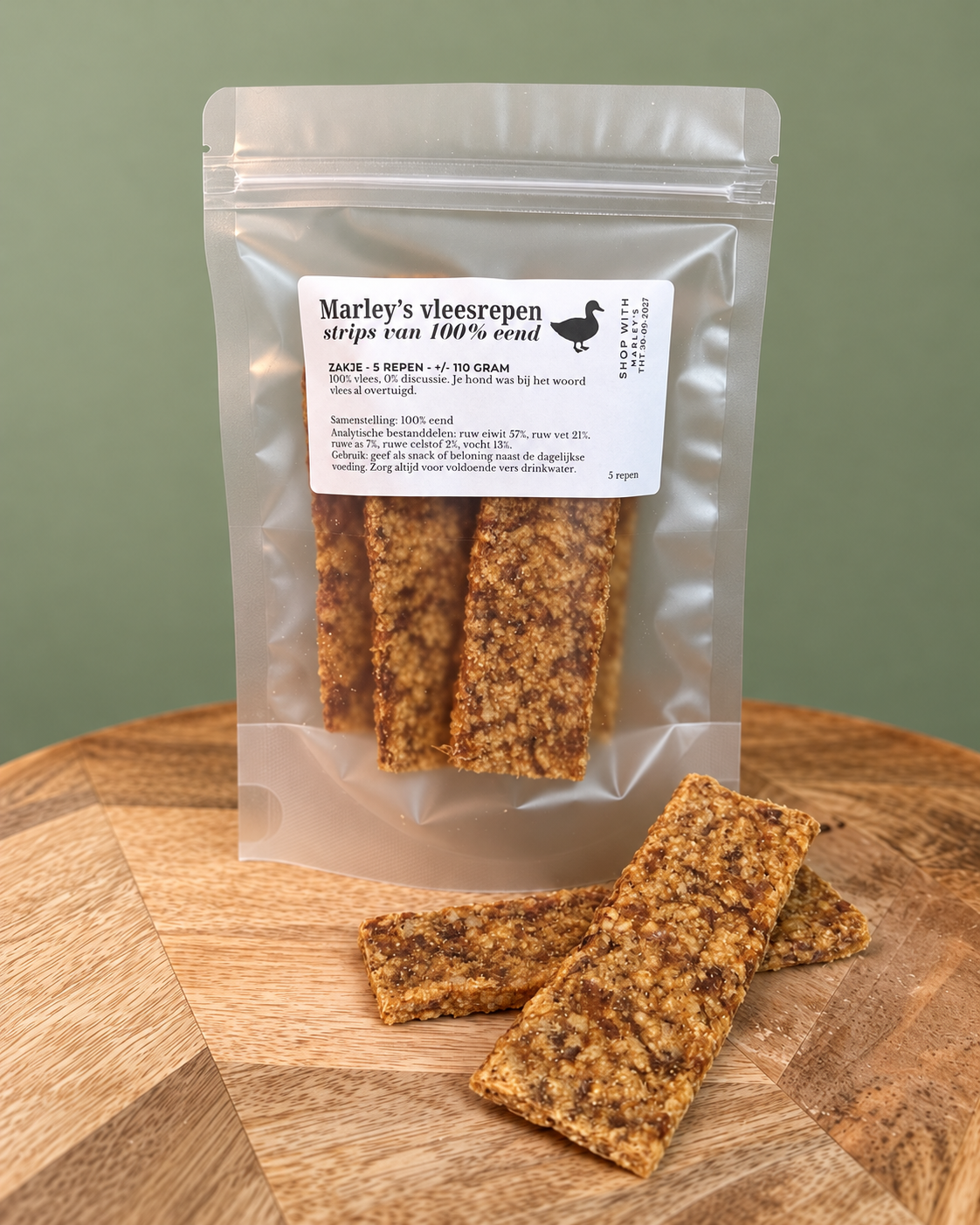 Marley’s vleesrepen van 100% eend, vijf gedroogde vleesrepen van circa 110 gram in hersluitbaar zakje op houten plateau met groene achtergrond